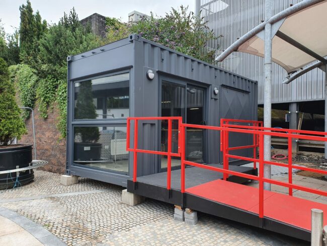 External view of container coffee shop with accessibility ramp and floor-length window.